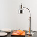 A Hanson Heat Lamps freestanding heat lamp with a chrome finish over a table with plates and a piece of ham.
