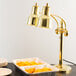 A Hanson Heat Lamps brass freestanding heat lamp with dual bulbs over a table with food in a tray.