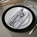 A white Charge It by Jay plastic charger plate with silverware and a napkin on it.