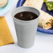 A Shimmering Silver plastic cup of liquid next to a burrito on a table.