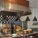 A ceiling mount Hanson Heat Lamp with a black finish heating a large metal container of food in a commercial kitchen.
