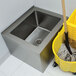 A stainless steel floor mounted mop sink with a mop and bucket.