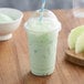 A green smoothie made with Big Train Dragonfly Honeydew Blended Creme Frappe mix in a plastic cup with a straw.
