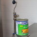 An Edlund standard duty manual can opener attached to a metal surface with an open can of pumpkin soup.