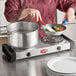 A woman cooking food in a pan on an Avantco double burner countertop range.