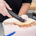 A person using a Zeroll Zerolon #30 black ice cream scoop to scoop ice cream.
