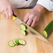 A person using a Mercer Culinary yellow chef knife to cut cucumbers.