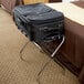 A black suitcase on a Lancaster Table & Seating chrome folding luggage rack.