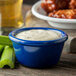 A blue bowl of white sauce next to celery sticks and chicken wings.