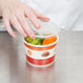 A hand putting vegetables into a Choice paper food container with a plastic lid.