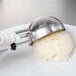A gloved hand uses a Vollrath white metal scoop to serve rice onto a white plate.