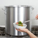 A person using a spoon to serve food from a Vollrath Wear-Ever stock pot.