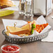 A Tablecraft gray oval platter basket holding a sandwich and fries.