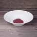 A white Elite Global Solutions large melamine bowl filled with red beans on a wood surface.