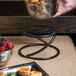 A hand uses an Elite Global Solutions round metal stand to hold a bowl of fruit on a table.