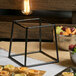 An Elite Global Solutions steel stand on a table with food and a bowl of fruit.