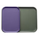 A purple Cambro cafeteria tray with a green insert on a counter next to a green Cambro cafeteria tray.