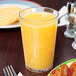 A clear plastic GET tumbler filled with orange juice next to a plate of food.
