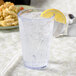 A GET clear plastic tumbler of water with ice and a lemon wedge.