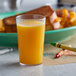 A clear plastic tumbler filled with orange juice on a table with crayons and a plate of food.