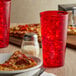 A plate of pizza and a red plastic tumbler filled with ice on a table.