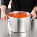 A person holding a large Vollrath Wear-Ever sauce pot of red sauce.