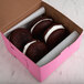 A close-up of three chocolate donuts in a pink bakery box.