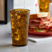 An amber plastic tumbler filled with ice tea next to a sandwich on a plate.