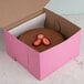 A chocolate cake in a pink bakery box with strawberries on top.