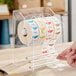 A clear plastic label dispenser with three rolls of day-of-the-week stickers.