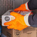 A person wearing orange San Jamar freezer gloves holding a box.