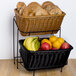 A black polyweave plastic basket filled with bread and fruit on a stand.