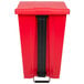 A red Rubbermaid rectangular plastic mobile step-on trash can with a black rectangular object.