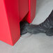 A person's foot stepping into a red Rubbermaid step-on trash container.