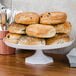 A Fineline white cake stand with a plate of bagels on it.
