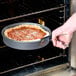 A person using a Thunder Group steel pan gripper to remove a pizza from the oven.