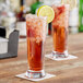 A tall, clear Acopa 16.25 oz. pilsner or cooler glass filled with a red beverage, ice, and garnished with a lemon slice.