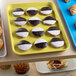 A yellow Cambro market tray on a table with pastries with white and chocolate icing.