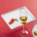 A CAC Bright White square party plate with a wine glass and two cherry tomatoes on a stemware tray.