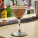 A clear martini glass filled with a creamy chocolate cocktail, placed on a bar counter.