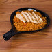 A CAC Festiware black fry pan plate with rice and chicken on it.