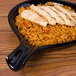 A CAC Festiware black fry pan plate with rice and chicken on it.