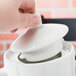 A hand using a Tuxton white China coffee pot lid on a white teapot.
