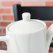A Tuxton Modena AlumaTux Pearl White china coffee pot lid on a white teapot.