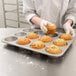 A person in a white coat putting a muffin in a Chicago Metallic jumbo muffin pan.