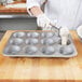 A person wearing gloves scooping dough into a Chicago Metallic Jumbo Pecan Roll / Muffin Pan.