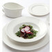 A white Tuxton China sauce bowl with a plate of salad and radish slices on it.