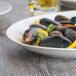 A white Tuxton oval china platter with mussels, lemon, and rosemary.
