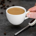 A hand holding a Tuxton AlumaTux Pearl White espresso cup filled with coffee.