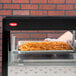 A person holding a tray of french fries in front of a Hatco countertop hot food display warmer.